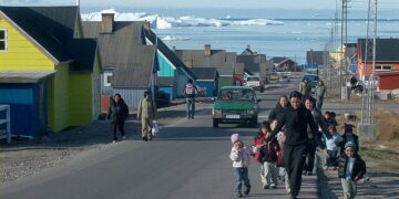 Daily life in a Greenlandic town with children walking and icebergs in the background, representing the culture and people affected by geopolitical tensions
