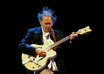 Legendary musician Neil Young performing live on stage with flowing hair, representing his 62-year musical catalog gifted to Greenland