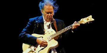 Legendary musician Neil Young performing live on stage with flowing hair, representing his 62-year musical catalog gifted to Greenland