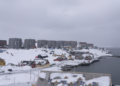 A snowy view of Nuuk, Greenland, featuring traditional colorful houses and modern apartment buildings under an overcast sky
