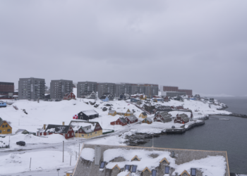 A snowy view of Nuuk, Greenland, featuring traditional colorful houses and modern apartment buildings under an overcast sky