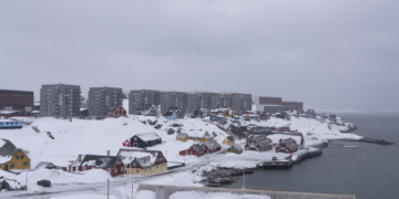 A snowy view of Nuuk, Greenland, featuring traditional colorful houses and modern apartment buildings under an overcast sky