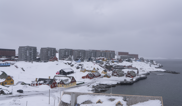 A snowy view of Nuuk, Greenland, featuring traditional colorful houses and modern apartment buildings under an overcast sky
