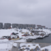 A snowy view of Nuuk, Greenland, featuring traditional colorful houses and modern apartment buildings under an overcast sky