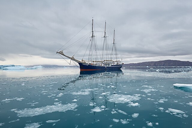 A large sailing ship navigating through ice floes in Disko Bay, Greenland
