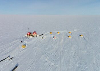 Aerial view of the EastGRIP scientific research camp on the vast, snow-covered Greenland ice sheet, showing yellow tents and a central research station, illustrating the sites where international climate collaboration is at risk