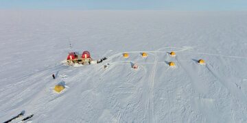 Aerial view of the EastGRIP scientific research camp on the vast, snow-covered Greenland ice sheet, showing yellow tents and a central research station, illustrating the sites where international climate collaboration is at risk