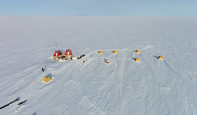 Aerial view of the EastGRIP scientific research camp on the vast, snow-covered Greenland ice sheet, showing yellow tents and a central research station, illustrating the sites where international climate collaboration is at risk