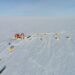 Aerial view of the EastGRIP scientific research camp on the vast, snow-covered Greenland ice sheet, showing yellow tents and a central research station, illustrating the sites where international climate collaboration is at risk